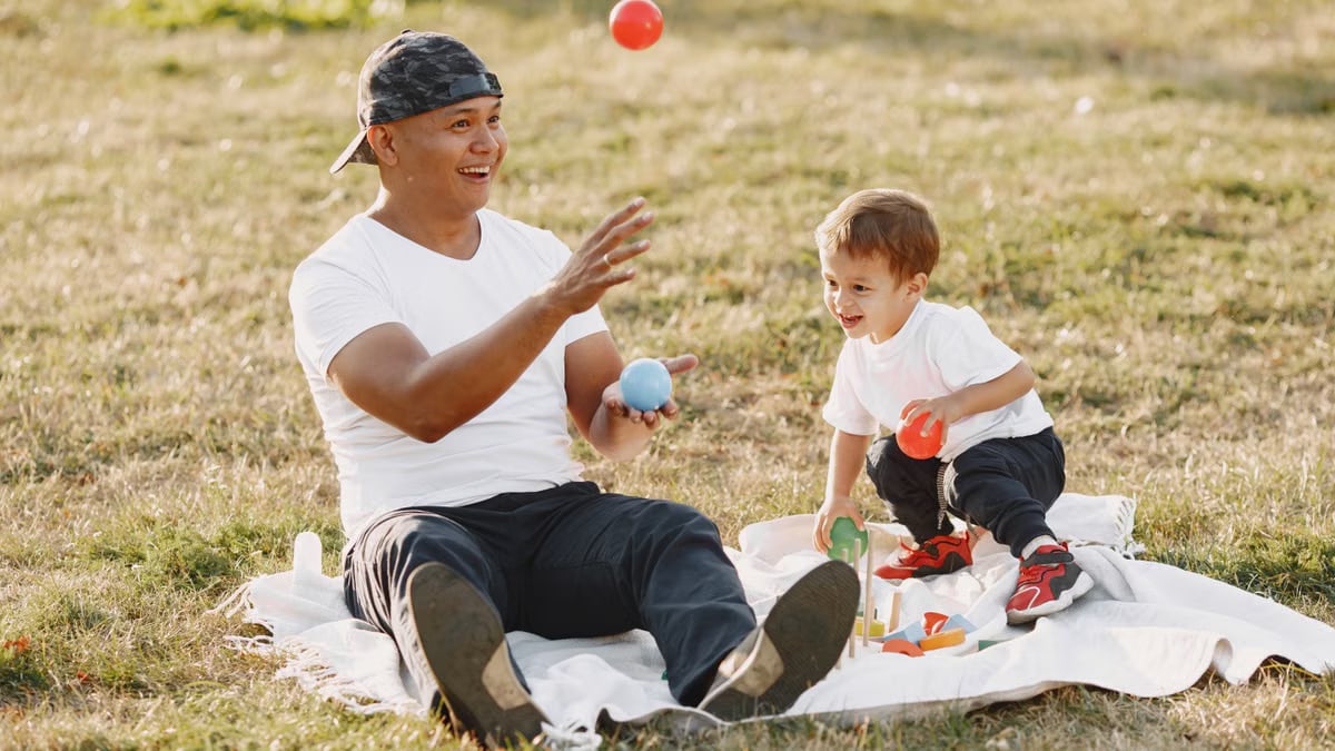 Father and son having fun while picnicking outdoors, playing with balls.
